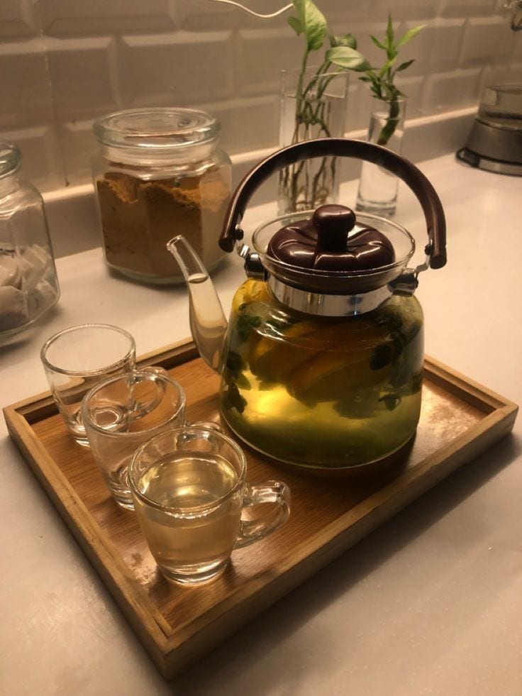 A glass teapot of brewed tea with small glass cups on a wooden tray