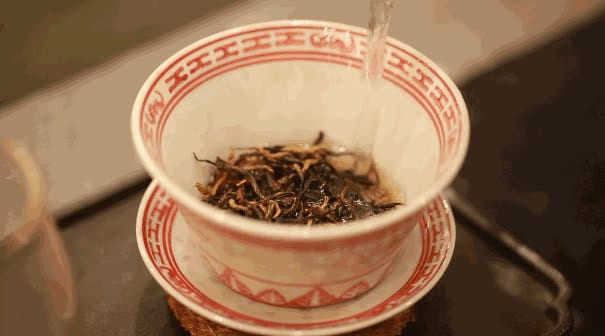 Hot water being poured over dry tea leaves in a porcelain gaiwan