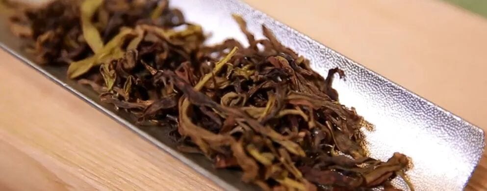 Dark twisted dry tea leaves arranged on a metal tea presentation tray