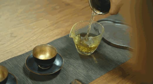 Tea being poured from a pot into a glass pitcher, with bubbles forming on the surface